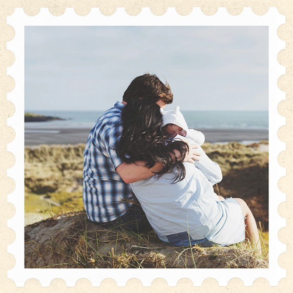 Image of an Irish family with a baby in embrace, sitting on the sand overlooking the ocean