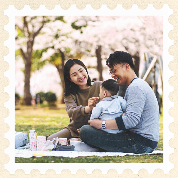 Image of a Japanese family sitting on a blanket with a baby under a blossoming cherry tree